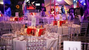 A room at Madame Tussauds full of tables and chairs set up for a dinner party. Wax figures of celebrities line the room as entertainment for the guests. Catering staff are also at the edges of the room ready to wait on the guests.